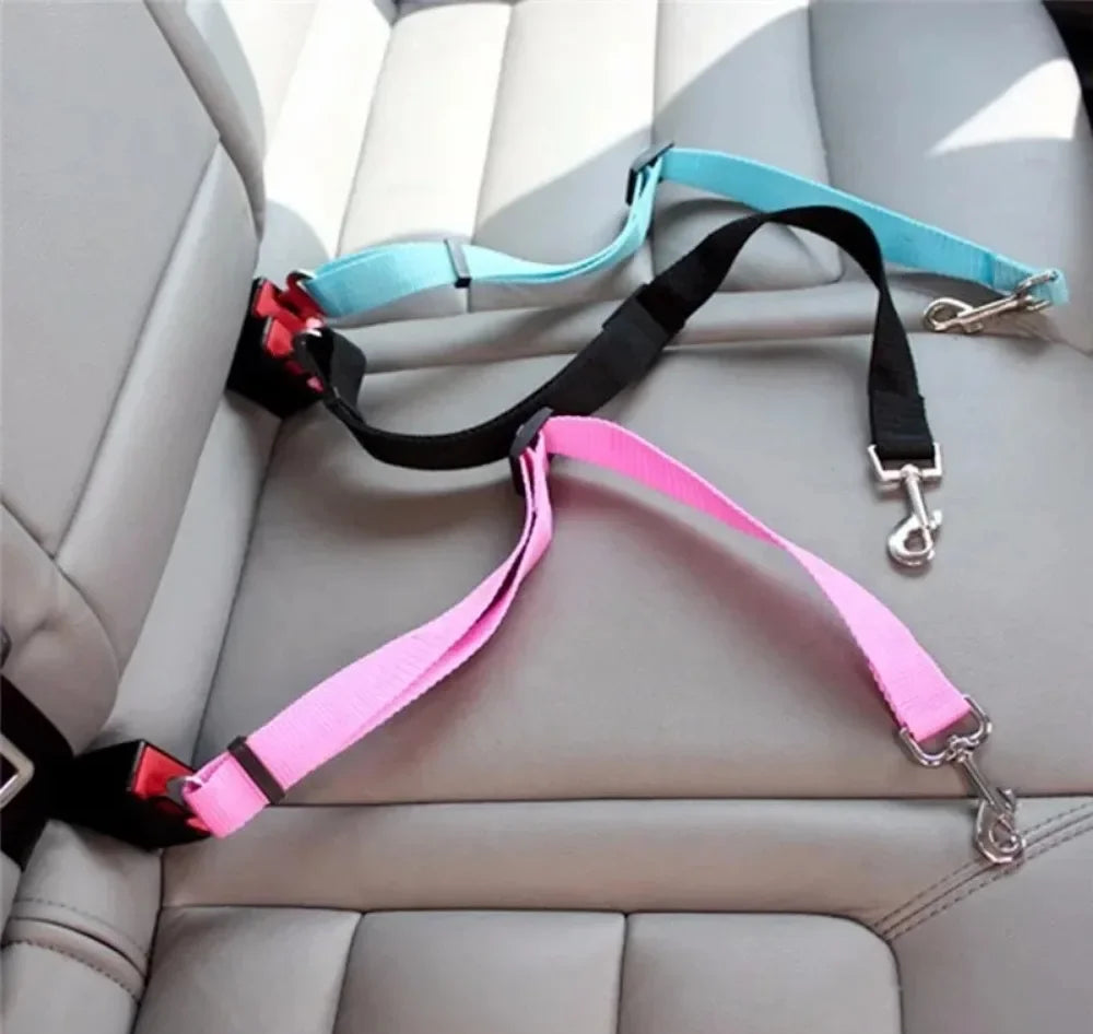 Two dog seat belts, one pink and one black with a blue handle, on a car seat.