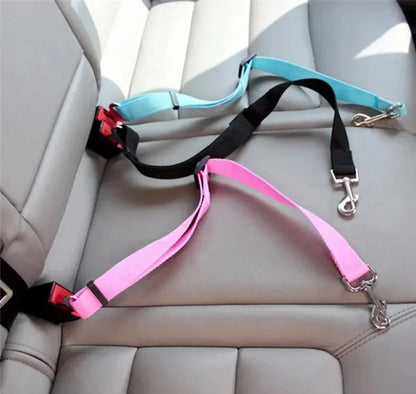 Two dog seat belts, one pink and one black with a blue handle, on a car seat.
